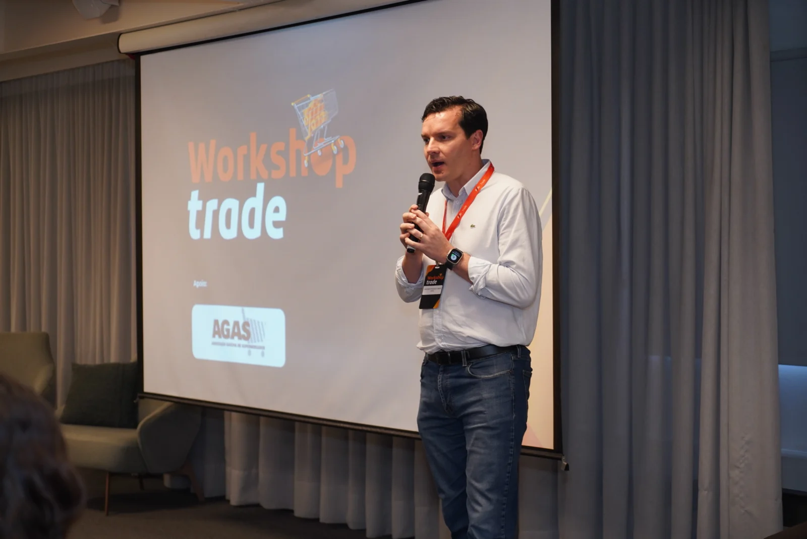 Palestrante fala ao microfone diante da tela do Workshop Trade